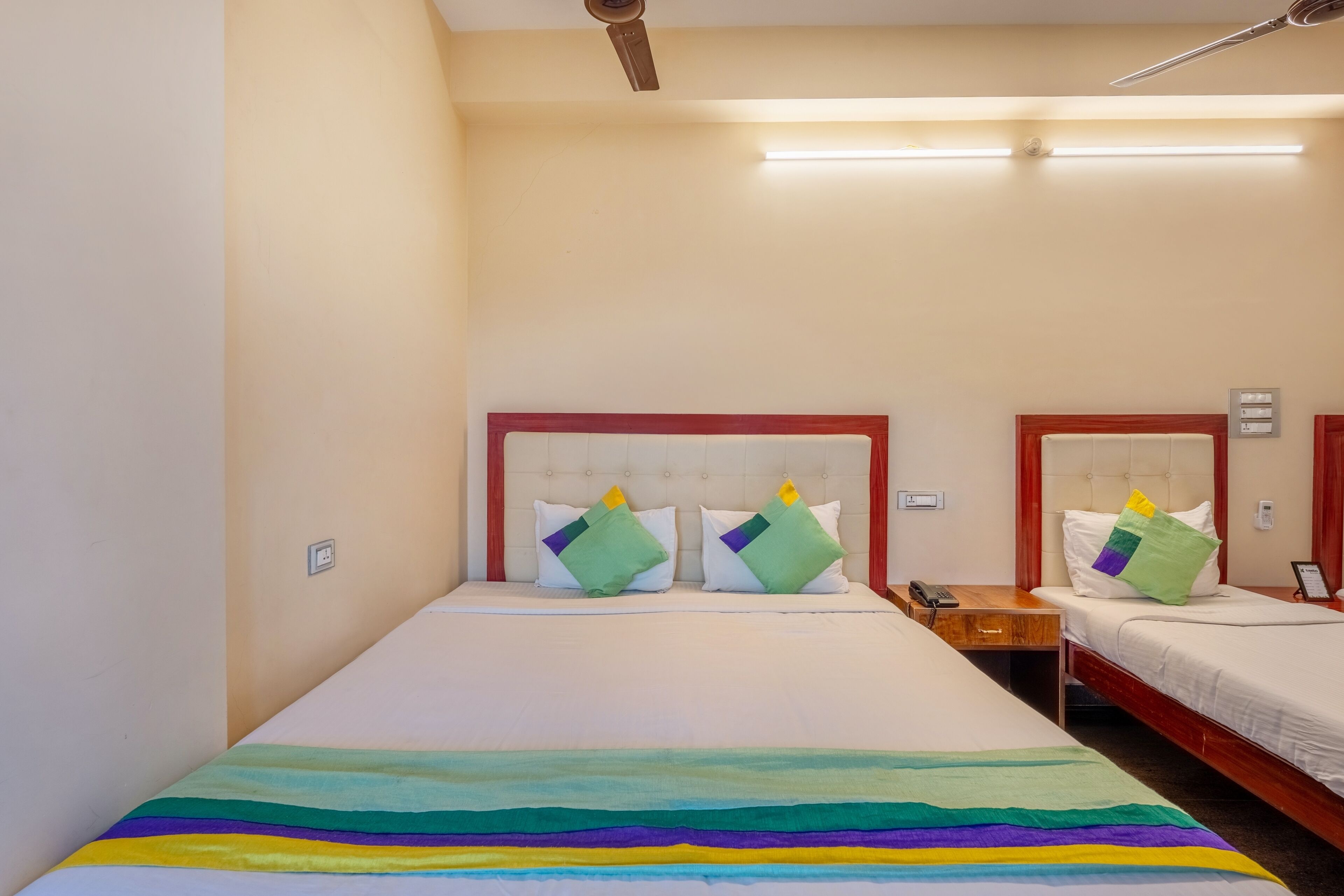 A hotel room with two beds, each with a wooden headboard and white bedding. There are bedside tables with lamps and a telephone on one side.