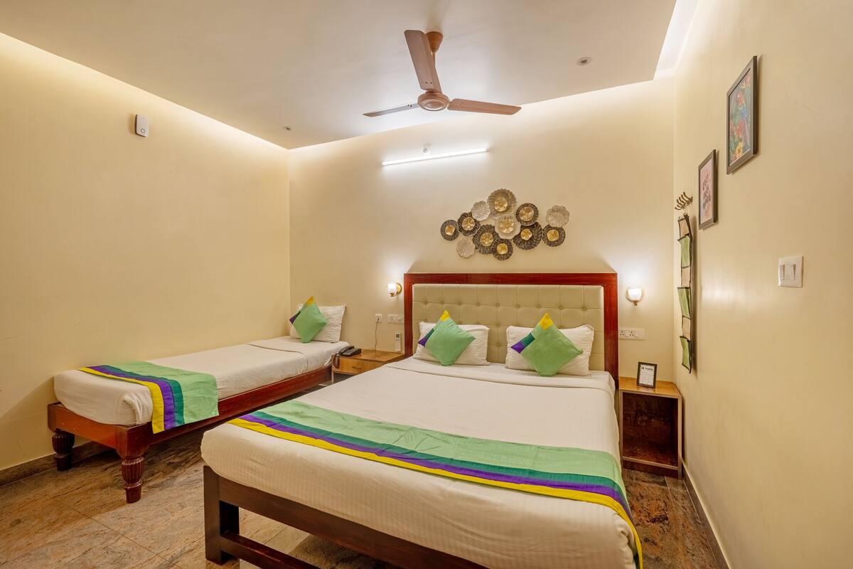 A hotel room with two single beds, a large bed, a ceiling fan, and a decorative wall piece.