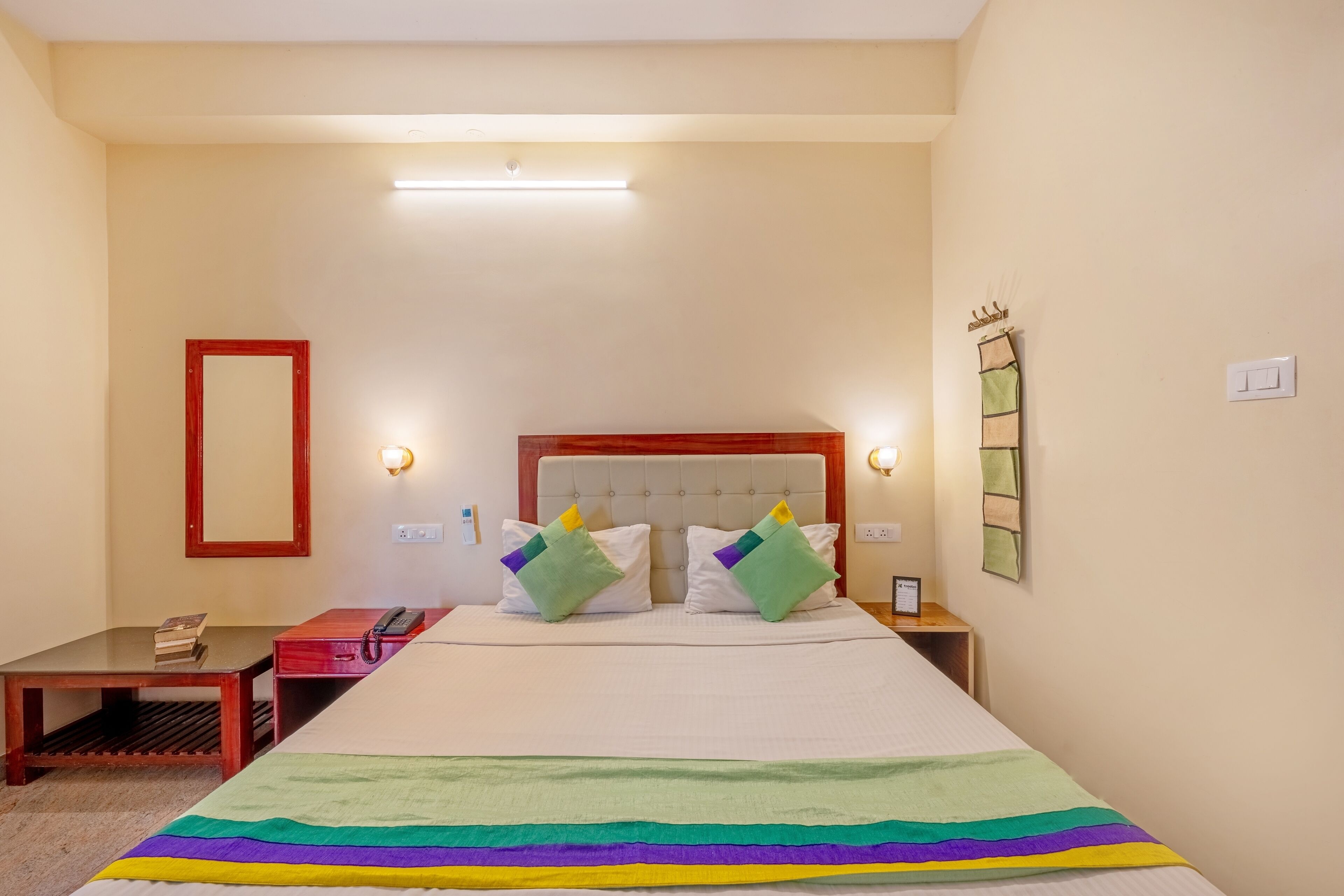 A hotel room with a bed, bedside tables, a mirror, and a bedside lamp.