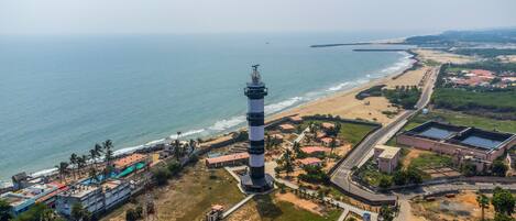 An aerial view of a coastal area with a prominent lighthouse, beach, and adjacent buildings.