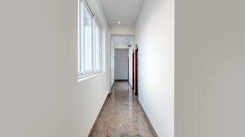 A narrow hallway with a marble floor, white walls, and a window on the left.