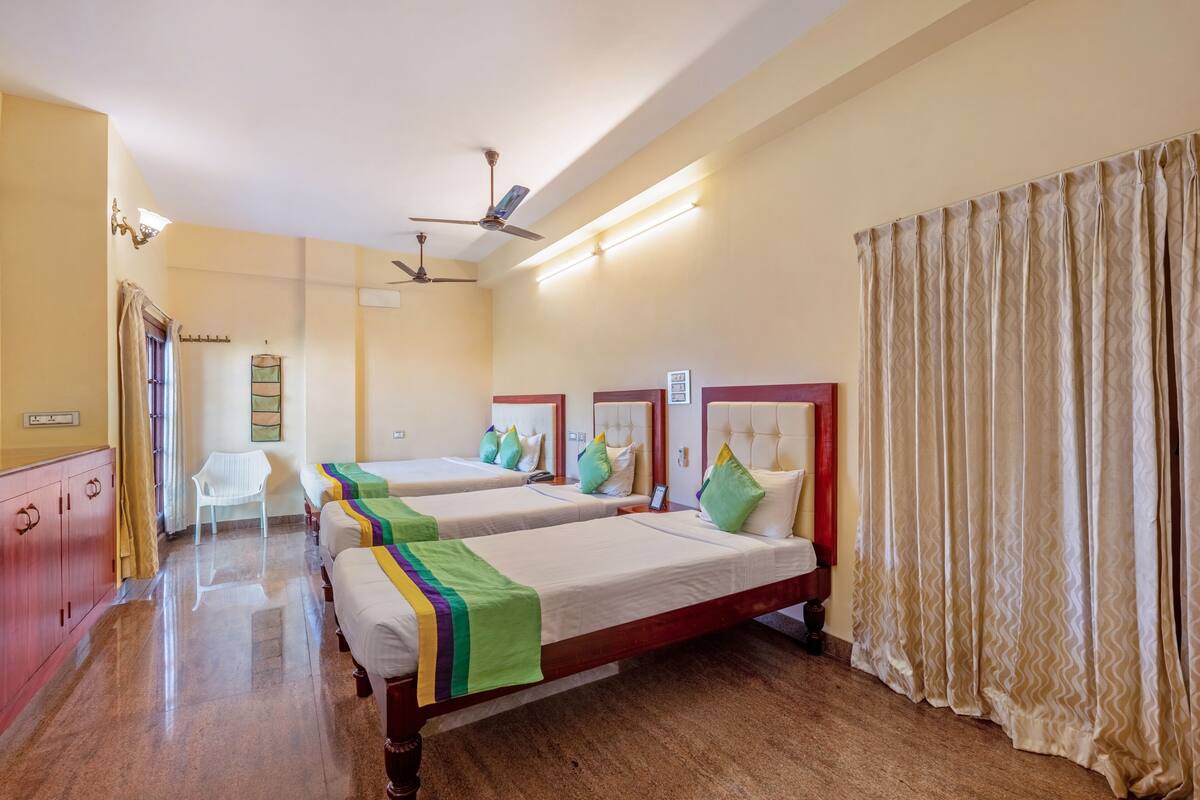 A hotel room with three beds, a wooden wardrobe, a white chair, and a ceiling fan.