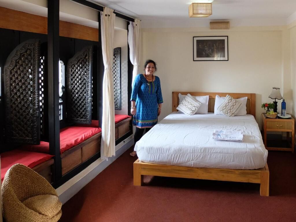A room with a bed, a wooden headboard, a nightstand, a lamp, and a window with curtains.