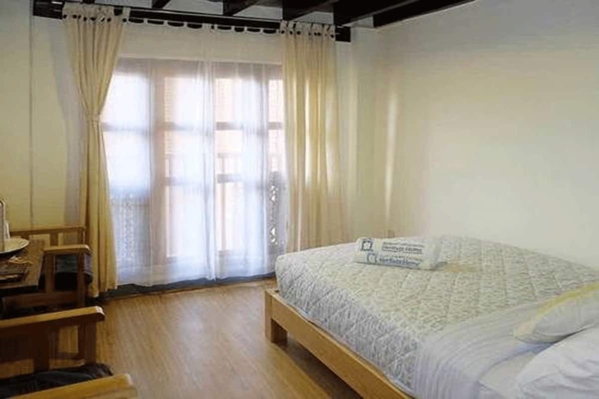 Un dormitorio con una cama de madera, un escritorio y una ventana con cortinas traslúcidas.