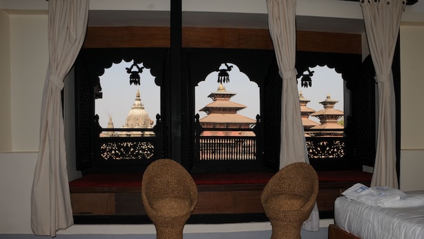 A room with a bed, two wicker chairs, and a window with a view of traditional pagodas. - Lalit Heritage Home (Lalitpur)