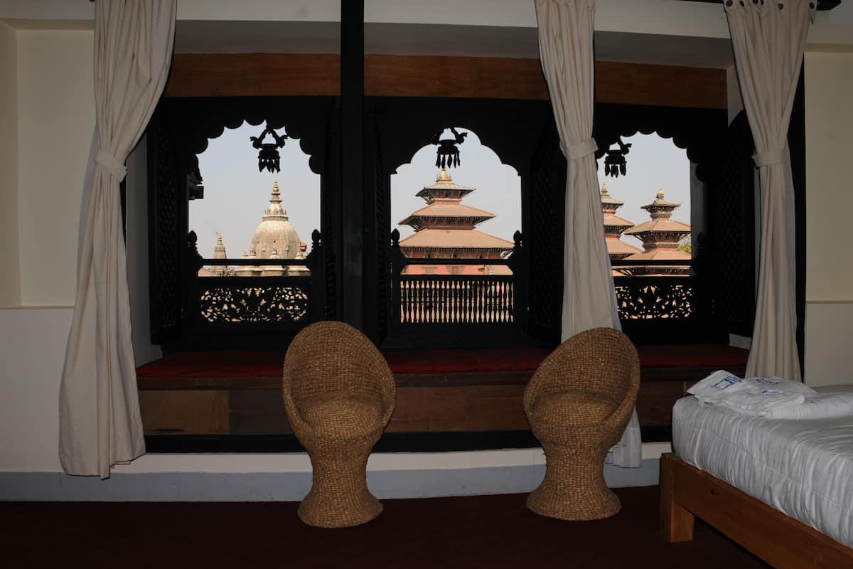 Una habitación con una cama, dos sillas de mimbre y una ventana con vistas a pagodas tradicionales.
