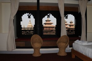 A room with a bed, two wicker chairs, and a window with a view of traditional pagodas.