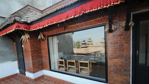 A traditional building with a tiled patio, a large window with a view of a pagoda, and a red decorative awning. - Lalit Heritage Home (Lalitpur)