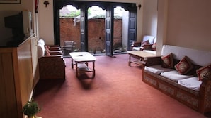 A cozy living room with a sofa, a table, and a TV on a cabinet. - Lalit Heritage Home (Lalitpur)
