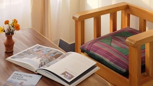 A wooden chair with a colorful cushion, a wooden table with a book titled "Practical Guide to Nepal," and a vase with flowers. - Lalit Heritage Home (Lalitpur)