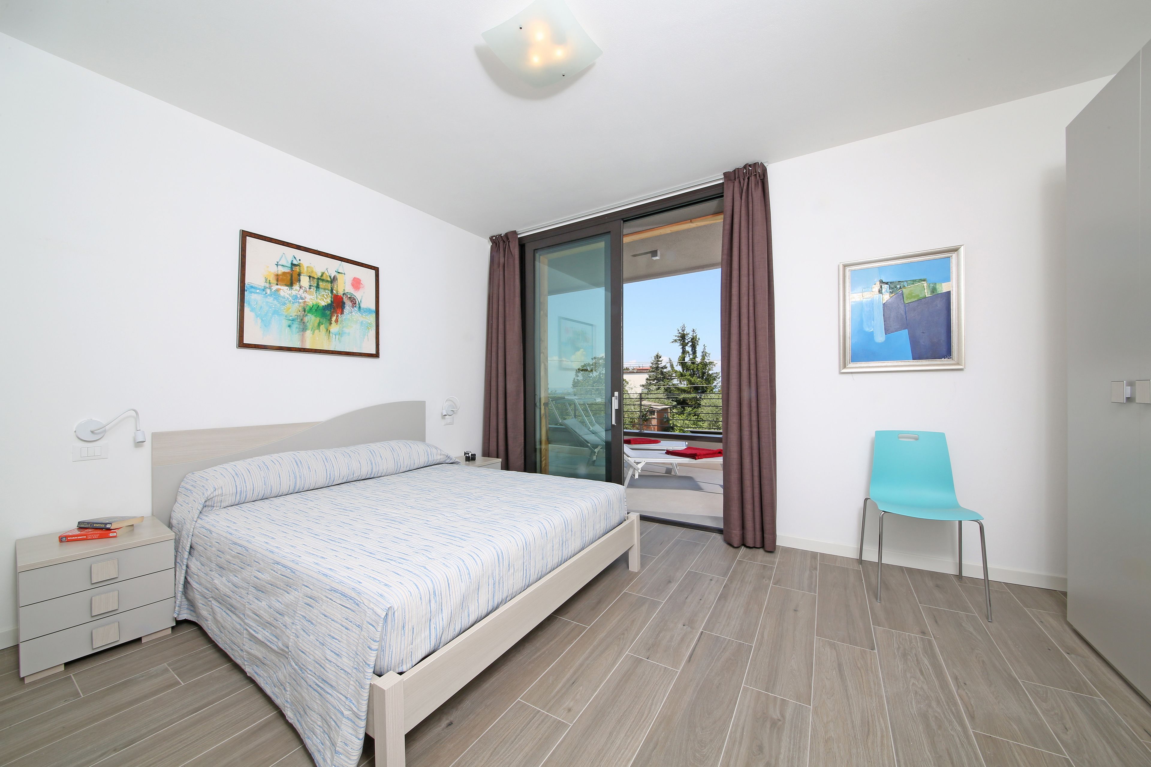 Une chambre à coucher comprenant un lit, une table de chevet, une chaise et une porte-fenêtre coulissante donnant sur un balcon.
