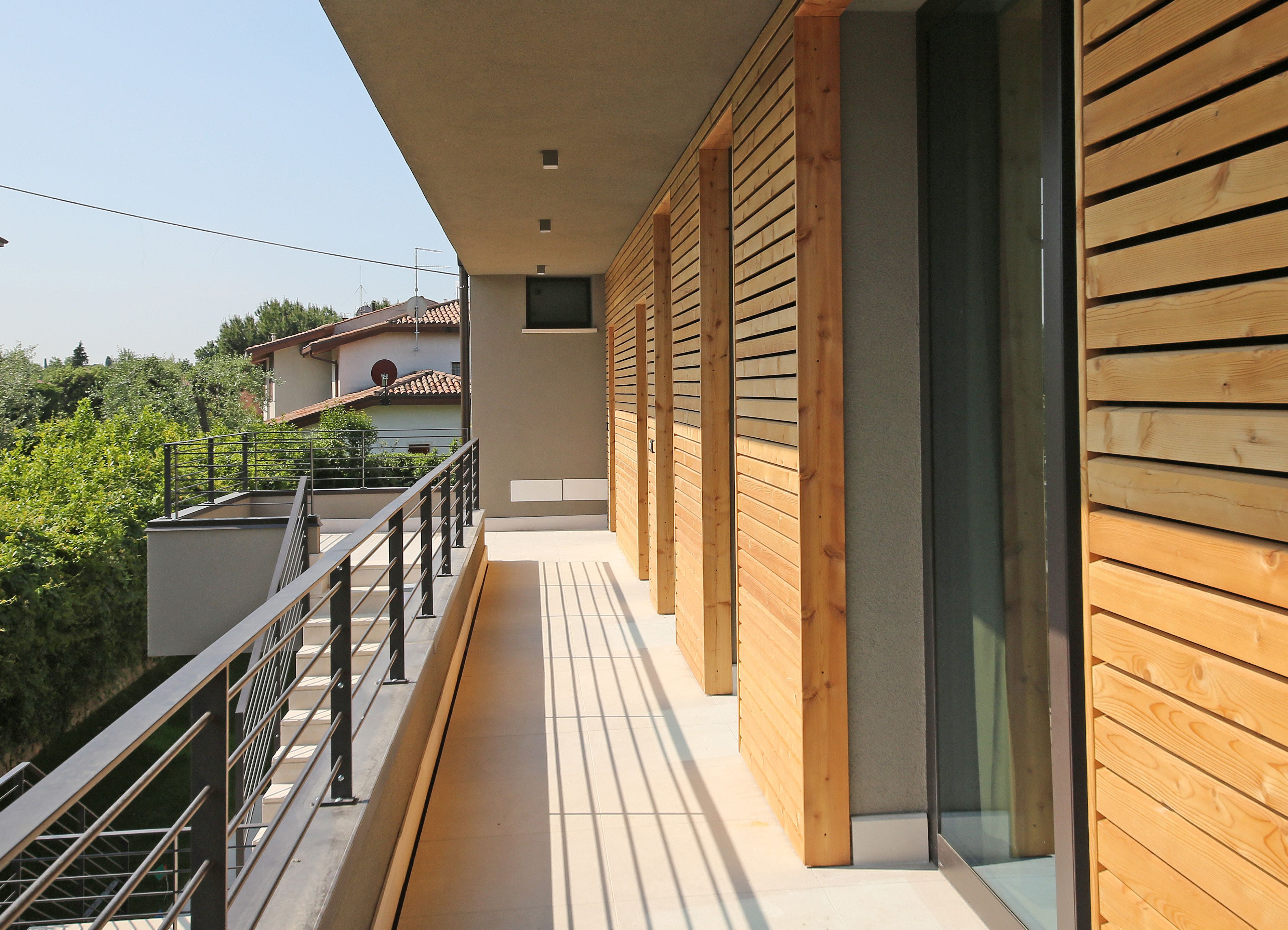 Ein moderner Balkon mit Holzlamellen, einem Metallgeländer und Blick auf ein Gebäude mit roten Ziegeldach.