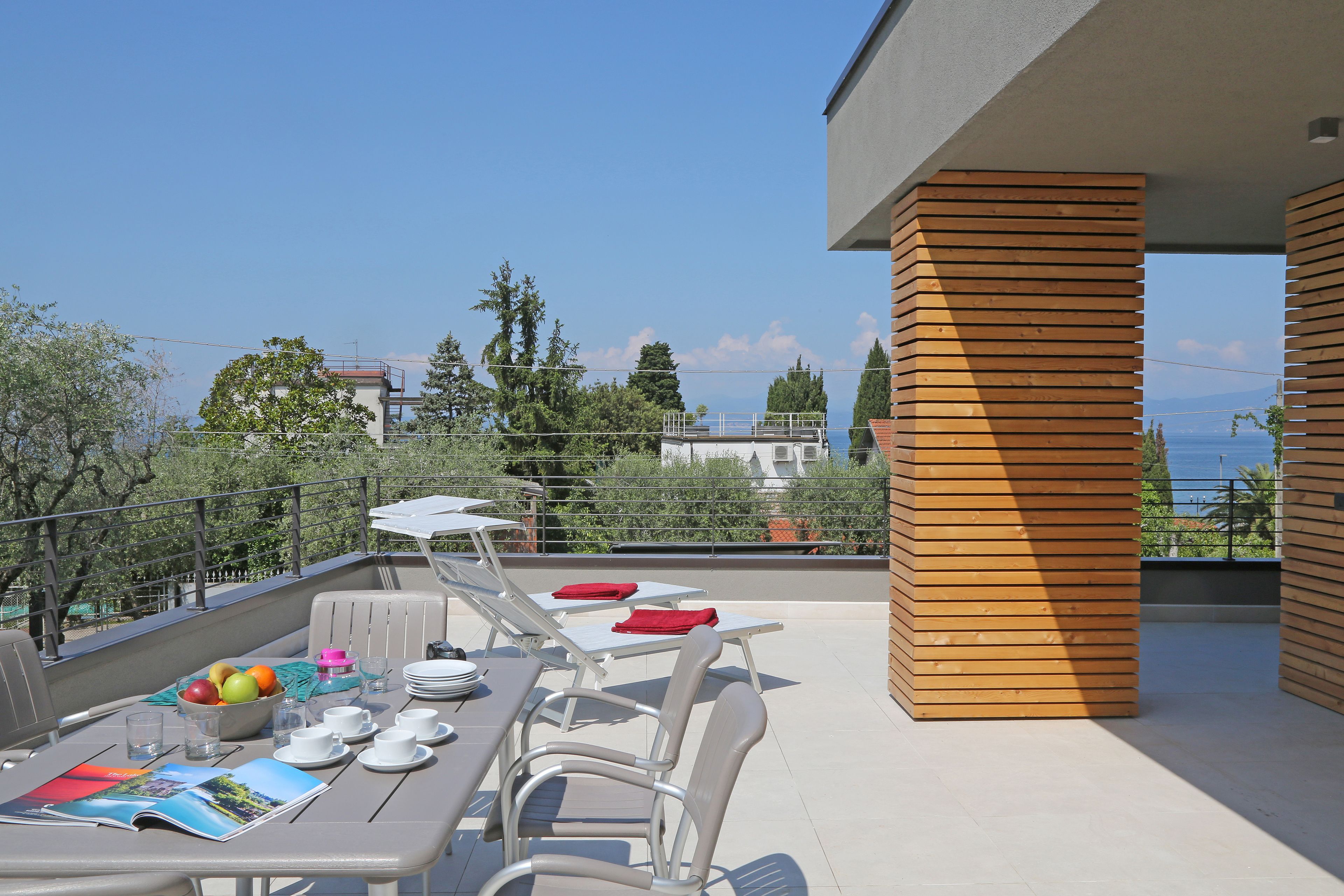 Una terrazza con tavolo apparecchiato per mangiare, poltrone relax e vista sul mare.