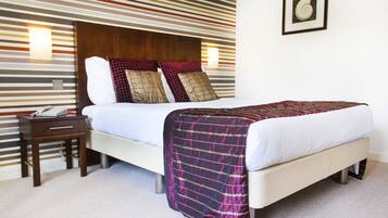 A neatly made bed with a patterned blanket, a bedside table with a phone, and a wall with a striped design and a framed picture.