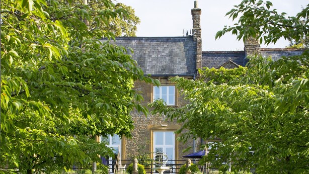 A stone building with a central staircase leading to a door, surrounded by well-maintained lawns and trees. - Lanes Hotel (Yeovil)