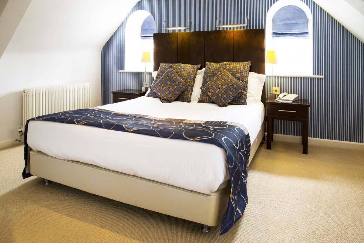 A bedroom with a large bed, two bedside tables, a nightstand, a window with a view, and a radiator.