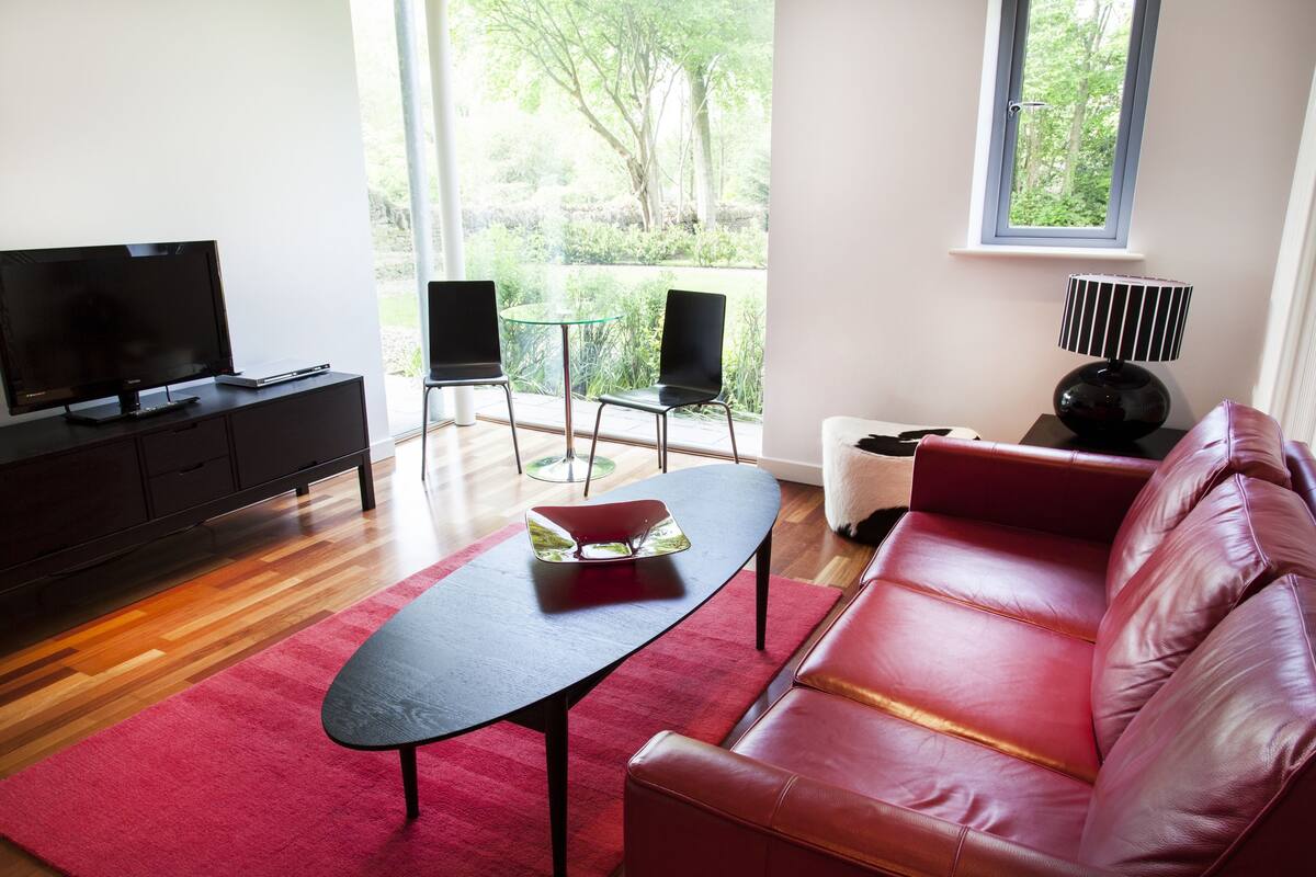 A modern living room with a leather sofa, a glass coffee table, a flat-screen TV, and a small table with chairs.