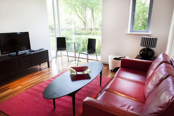 A modern living room with a leather sofa, a glass coffee table, a flat-screen TV, and a small table with chairs. - Lanes Hotel (Yeovil)