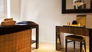 A hotel room with a massage table, a small desk with a mirror, and a chair.