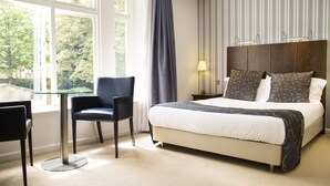 A hotel room with a large bed, a chair, a table, and a window with curtains. - Lanes Hotel (Yeovil)