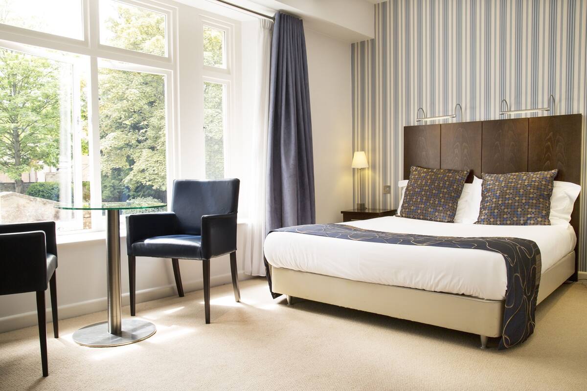 A hotel room with a large bed, a chair, a table, and a window with curtains.