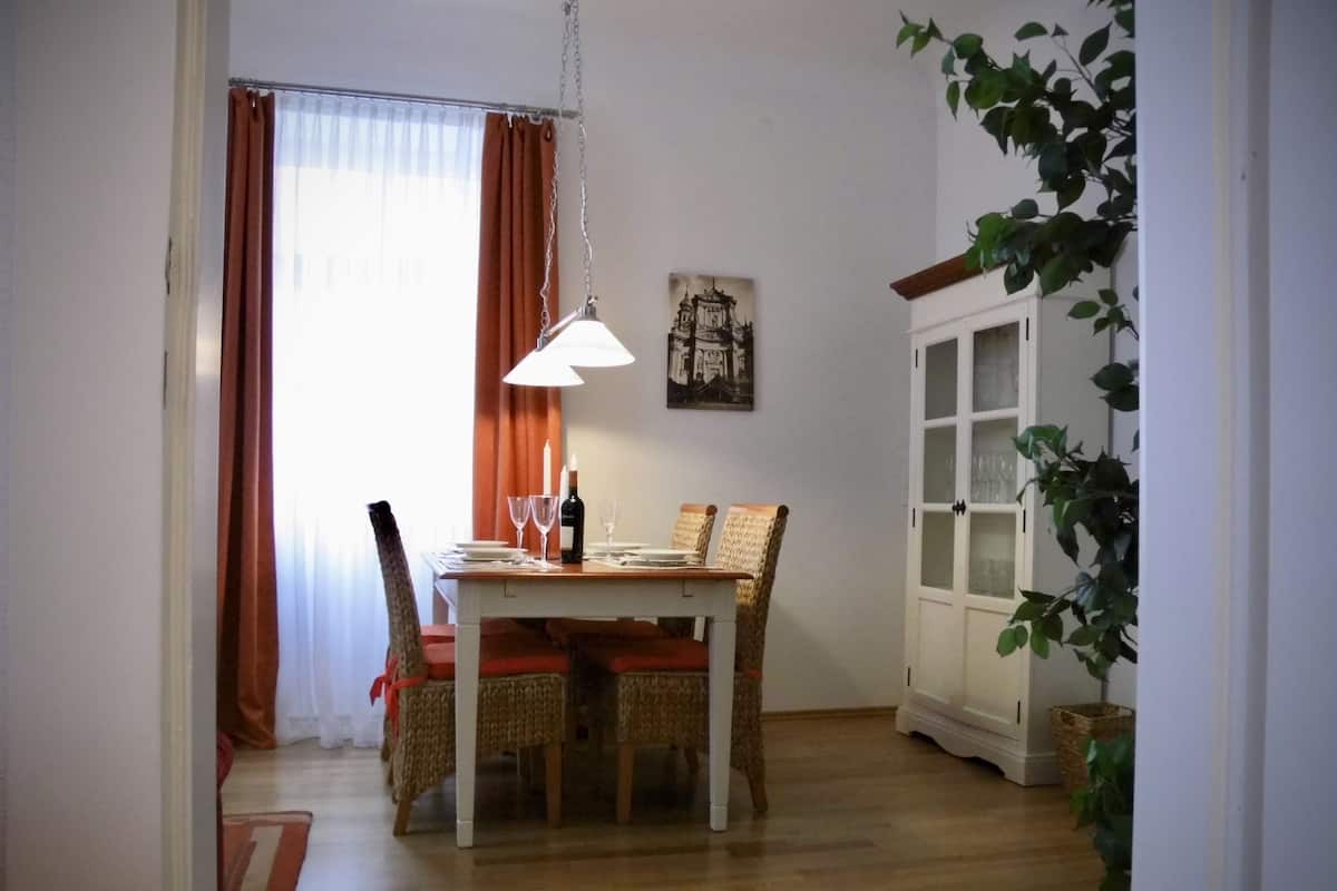 A dining area with a wooden table, wicker chairs, a hanging pendant light, and a white cabinet with glass doors.