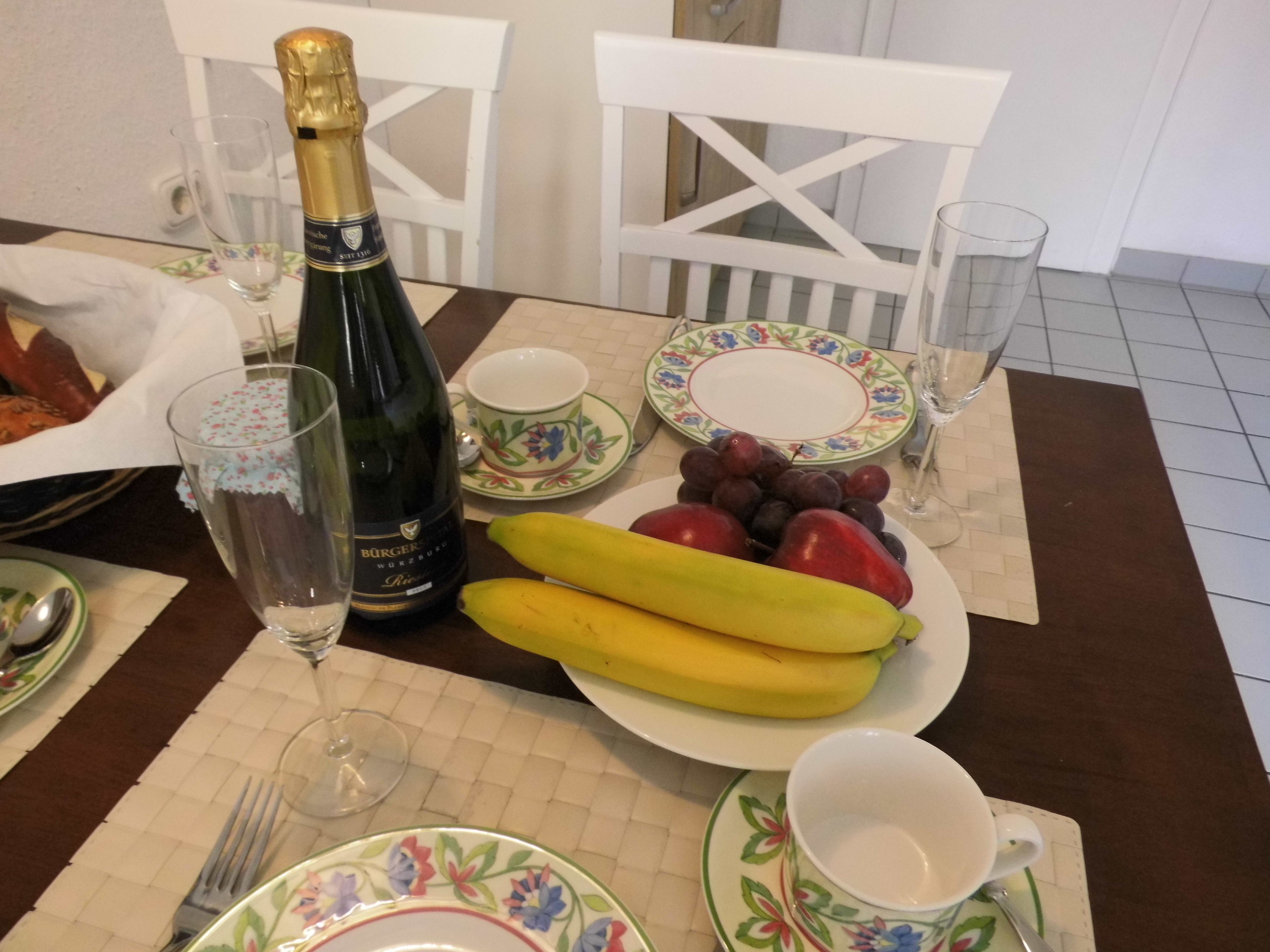 Ein Esstisch mit einer Champagnerflasche, einer Fruchtplatte und verschiedenen Geschirrteilen.