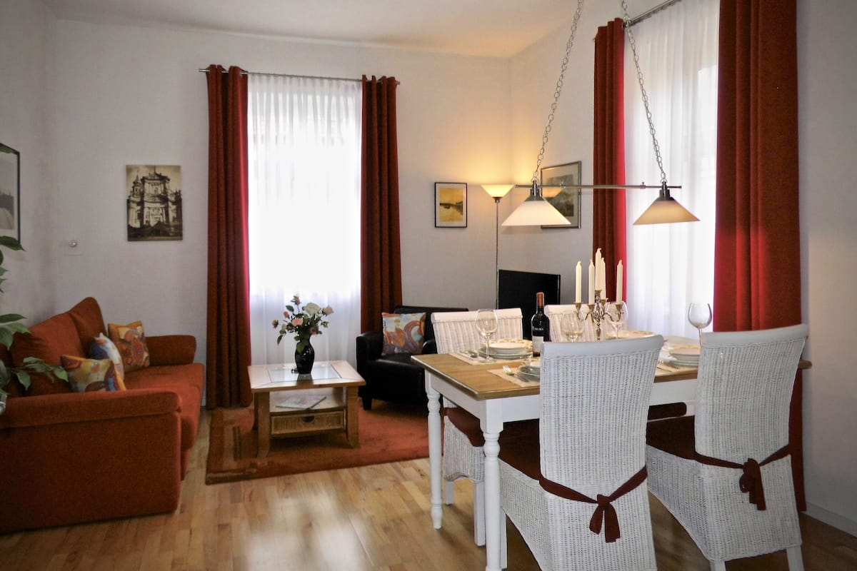 A dining area with a table set for four, surrounded by white wicker chairs with brown ribbons.