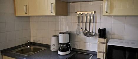A kitchen with a double sink, a coffee maker, a microwave, and hanging utensils.