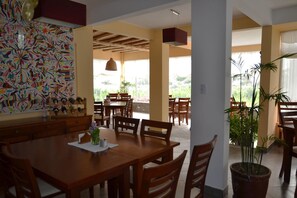 A dining area with wooden tables and chairs, a large decorative wall, and a potted plant. - Hotel Los Palomos (Lunahuana)
