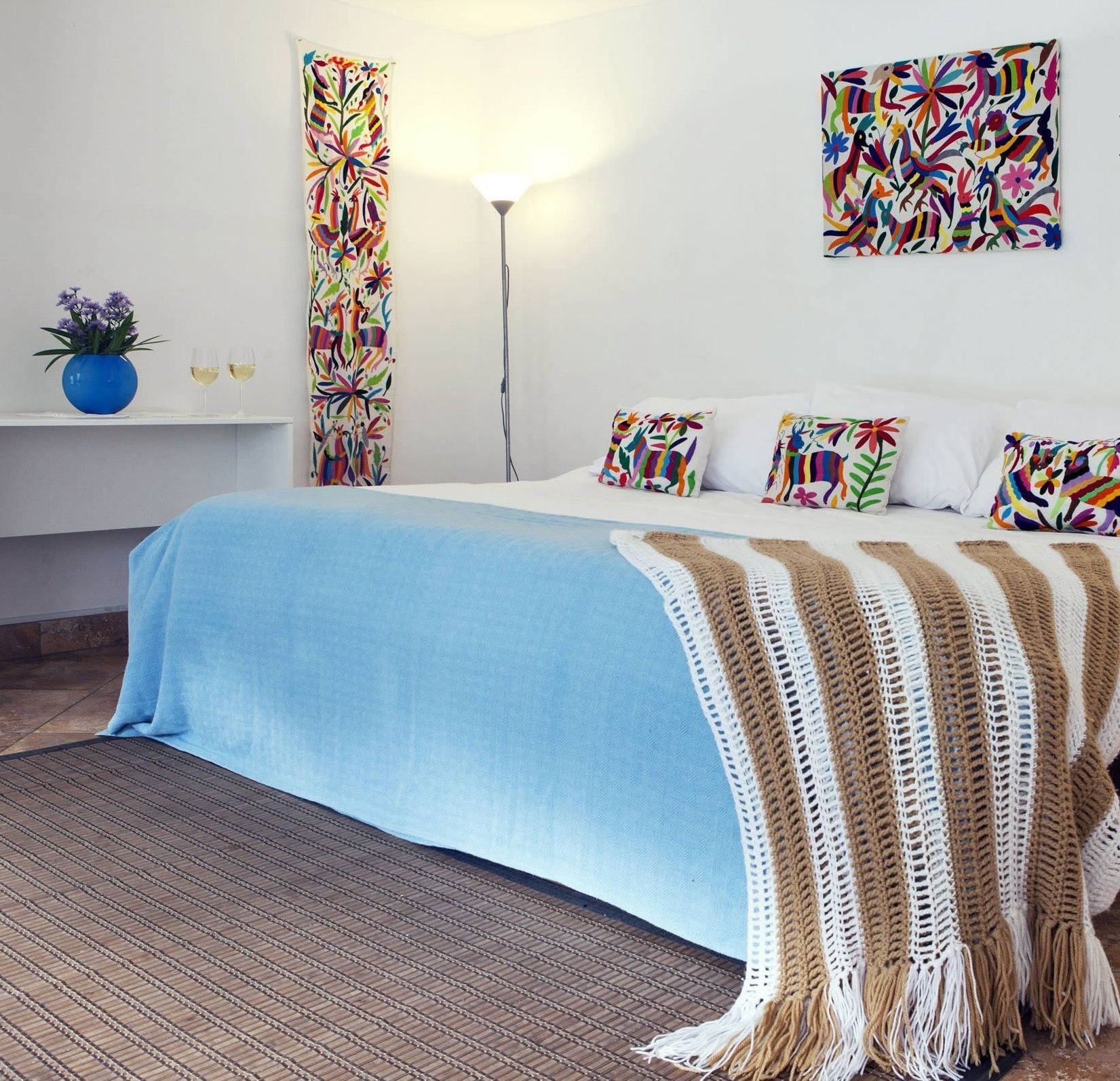 Un dormitorio con cama, almohadas, una lámpara y un cuadro de colores en la pared.