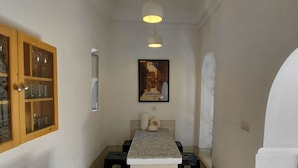A narrow hallway with a kitchen area, a wooden cabinet with glass doors, a framed picture on the wall, and a tiled floor. - Riad Dar Kleta (Marrakech)