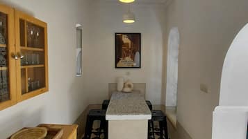 Un pasillo estrecho con una zona de cocina, un mueble de madera con puertas de cristal, un cuadro en la pared y piso de baldosas.
