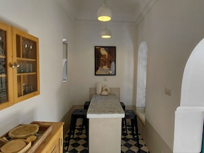 A narrow hallway with a kitchen area, a wooden cabinet with glass doors, a framed picture on the wall, and a tiled floor. - Riad Dar Kleta (Marrakech)