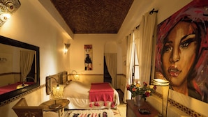 A hotel room with a bed, a mirror, a painting, a lamp, and a vase with flowers. - Riad Dar Kleta (Marrakech)