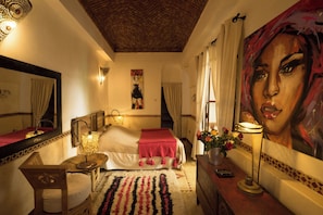 A hotel room with a bed, a mirror, a painting, a lamp, and a vase with flowers. - Riad Dar Kleta (Marrakech)