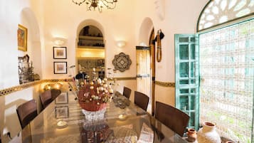 Un coin repas comprenant une table en verre, des chaises, un élément décoratif central et une vue par une fenêtre agrémentée d’un paravent décoratif.