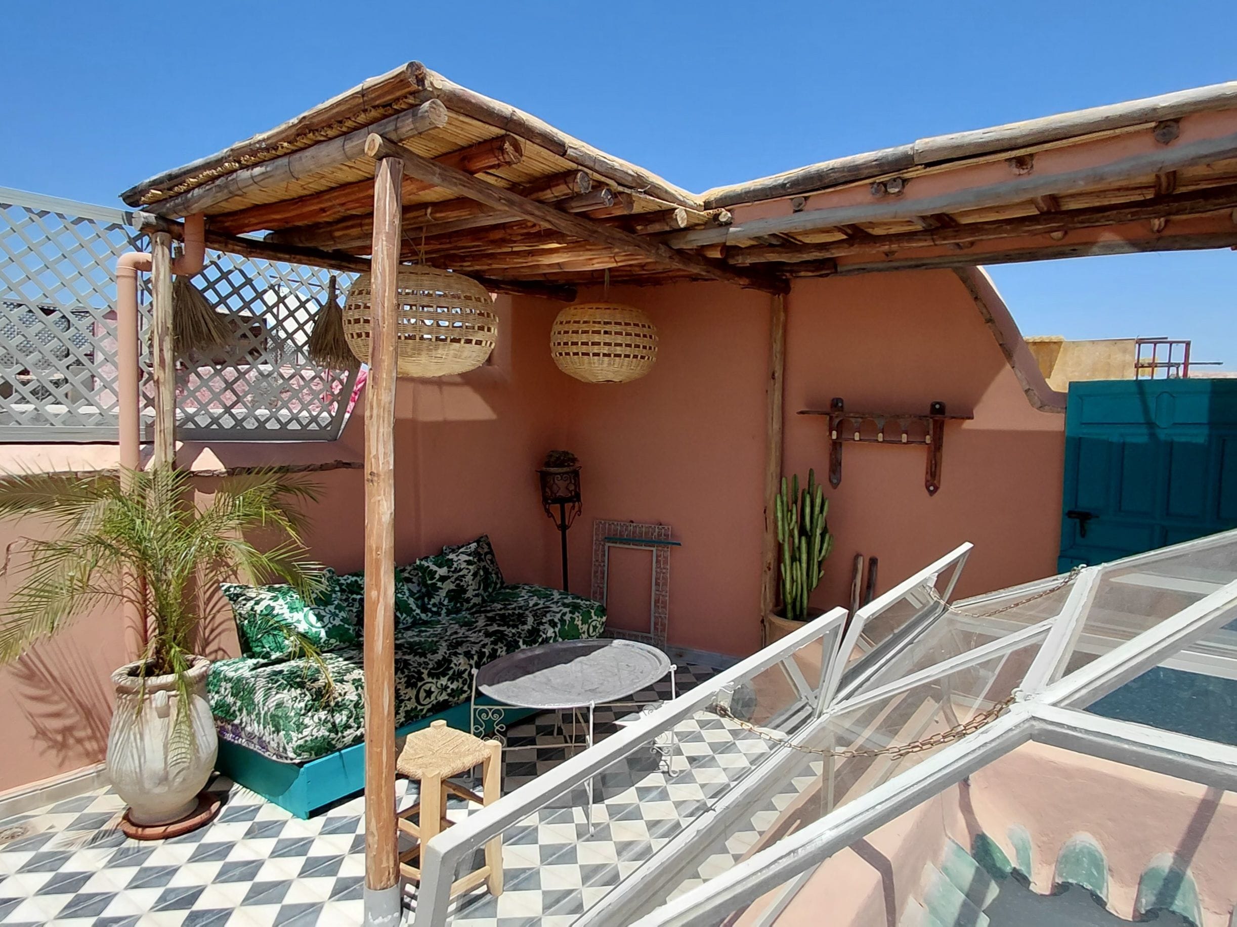 Una terraza en la azotea con una pérgola de madera, suelo a cuadros, una mesa redonda y un espacio de estar con cojines estampados.