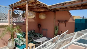 Una terraza en la azotea con una pérgola de madera, suelo a cuadros, una mesa redonda y un espacio de estar con cojines estampados.
