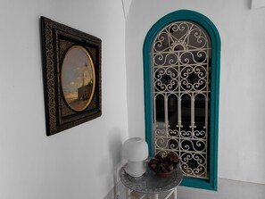 A framed painting, a decorative window, and a small table with a white vase and a bowl of chocolates. - Riad Dar Kleta (Marrakech)