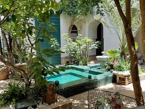 A courtyard with a swimming pool, potted plants, and a traditional building with arched doorways. - Riad Dar Kleta (Marrakech)