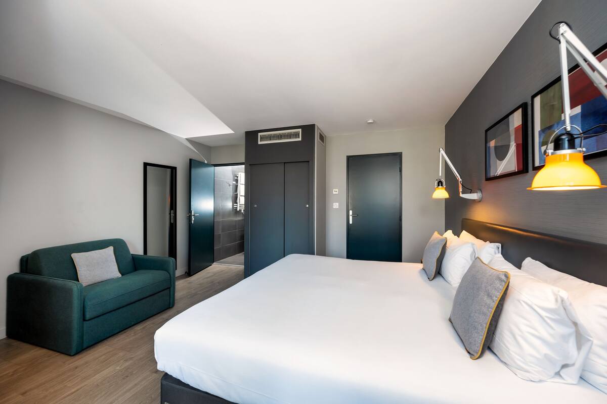 Une chambre d’hôtel moderne avec un grand lit, un canapé vert et un bureau.
