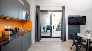 Une cuisine moderne équipée d’un four à micro-ondes, d’un grille-pain et d’une bouilloire, un coin repas avec une table et des chaises, et un téléviseur fixé au mur.