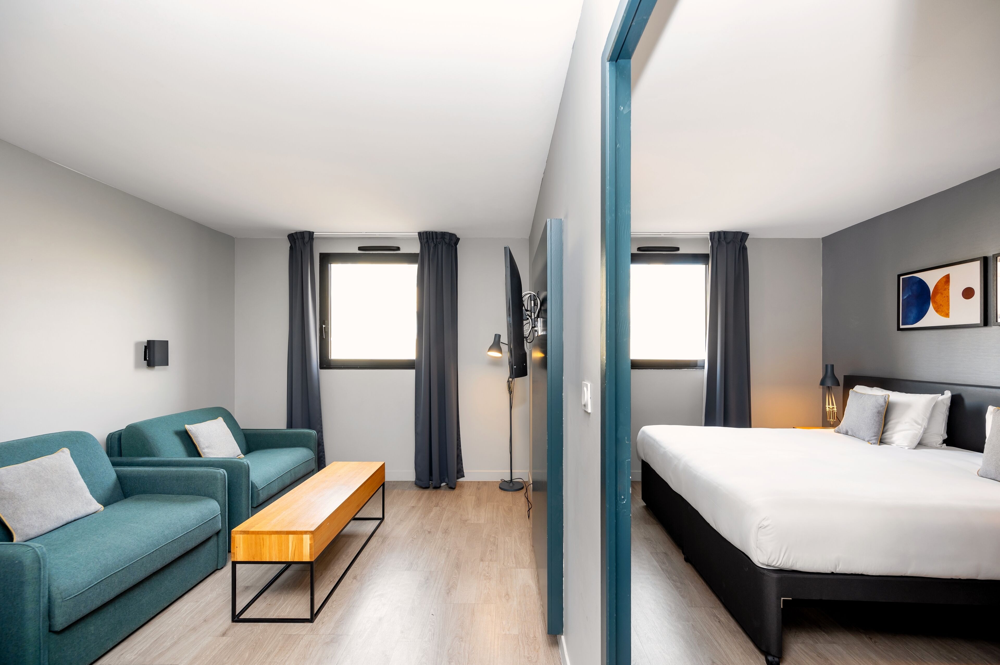 A modern hotel room with a bed, two sofas, a wooden bench, and a floor lamp.