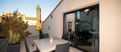 An outdoor patio with a table and chairs, a potted plant, and a yellow umbrella.