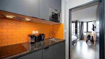 A modern kitchen with grey cabinets, an orange-tiled backsplash, a built-in microwave, and a coffee maker.
