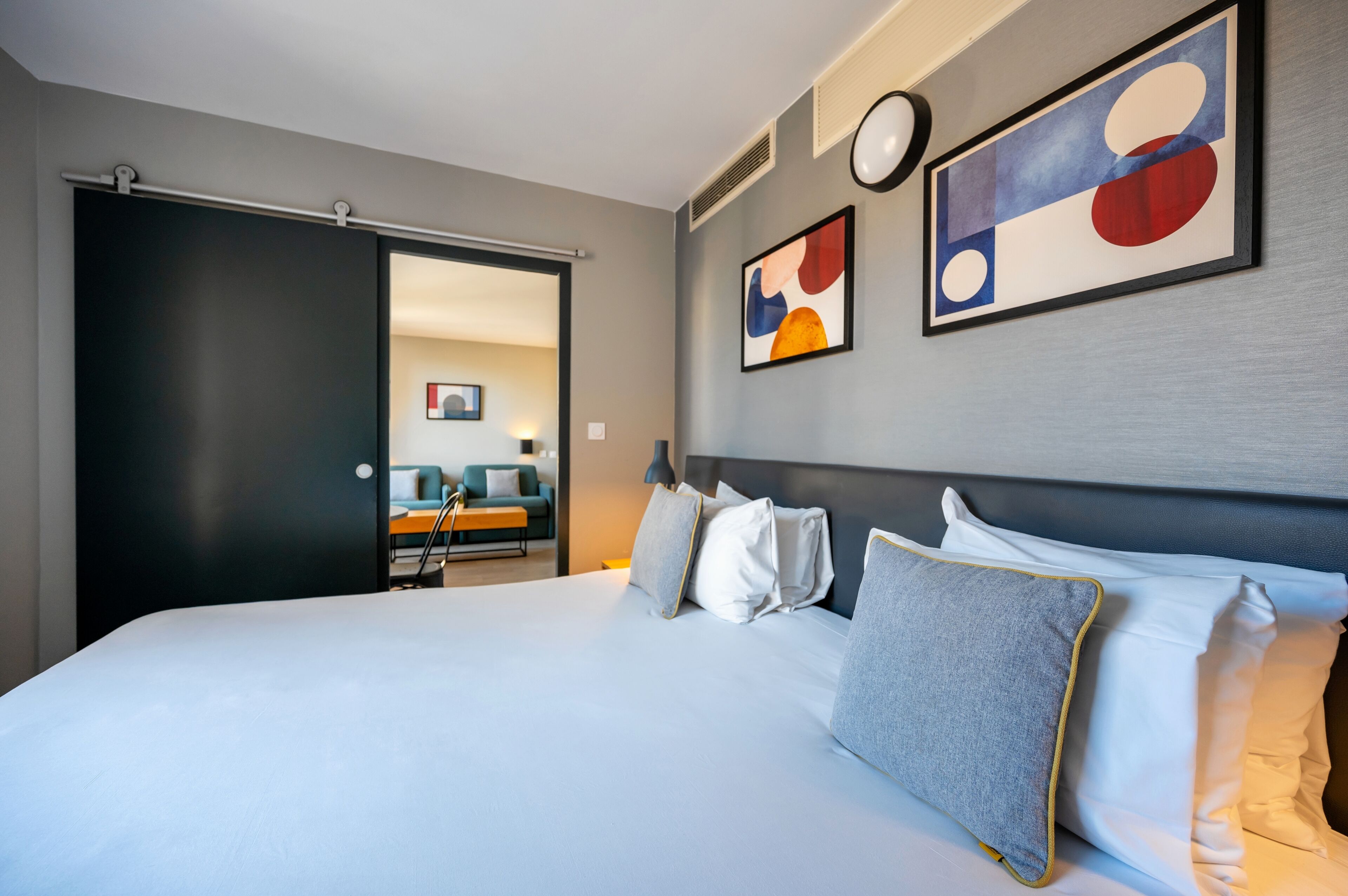 A modern hotel room with a large bed, a dark sliding door, and abstract art on the walls.