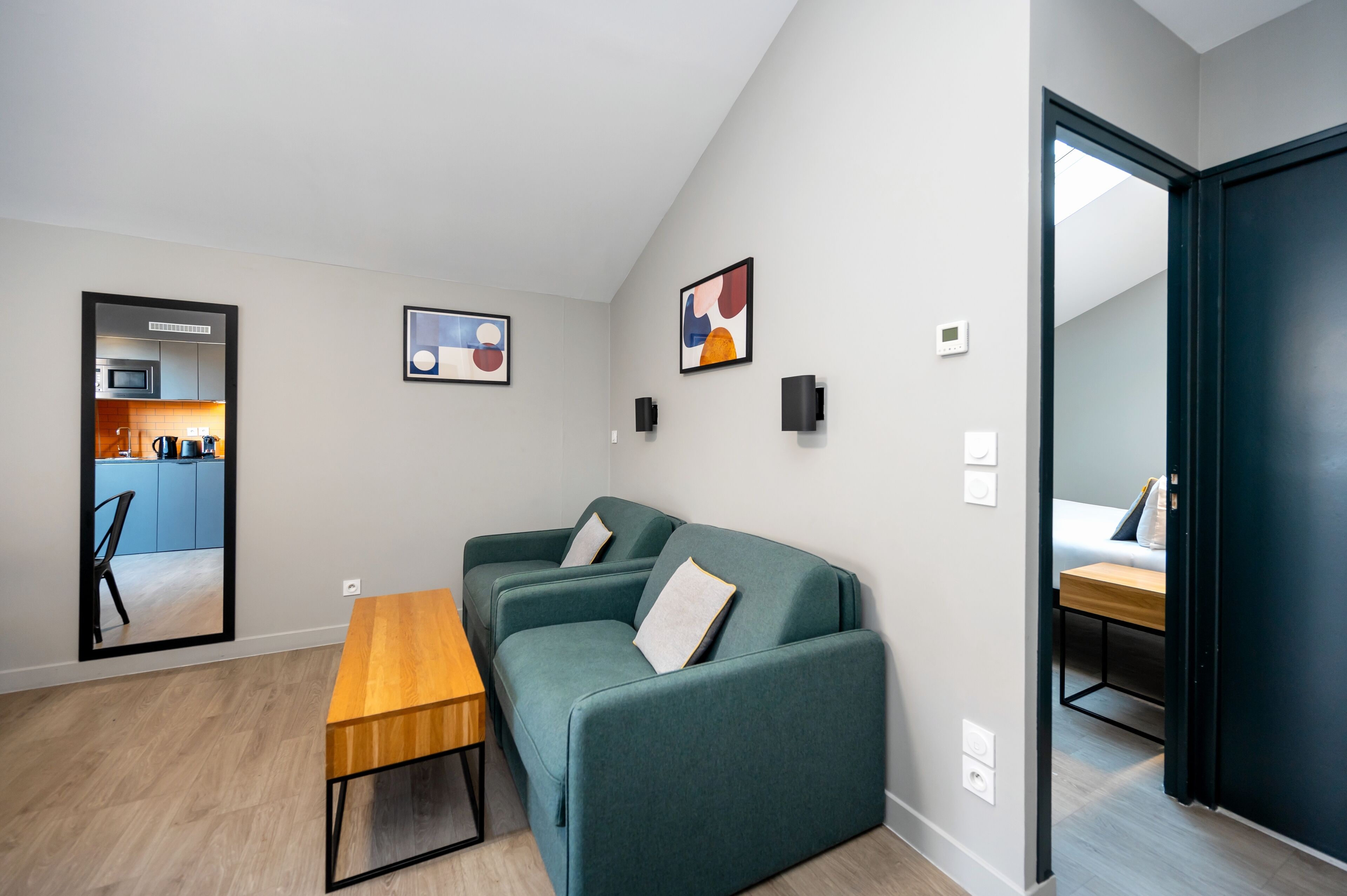 Een moderne woonkamer met een groene bank, een houten tafel en een keuken die door een open deur zichtbaar is.