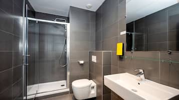 Une salle de bain moderne avec une douche à parois de verre, des toilettes blanches et un grand lavabo surmonté d’un miroir.