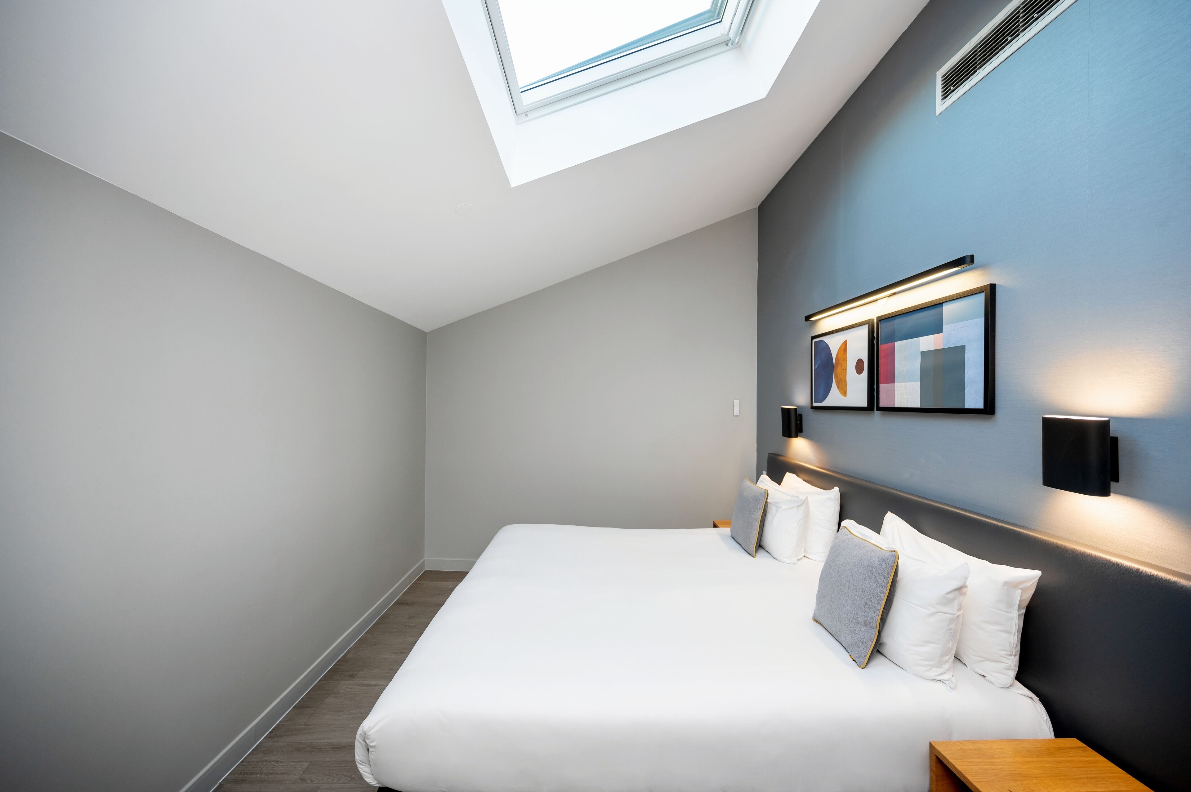 Une chambre moderne avec une lucarne, un grand lit et des luminaires fixés au mur.